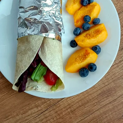 Tortilla z warzywami zawinięta na wynos, obok brzoskwinia i borówki