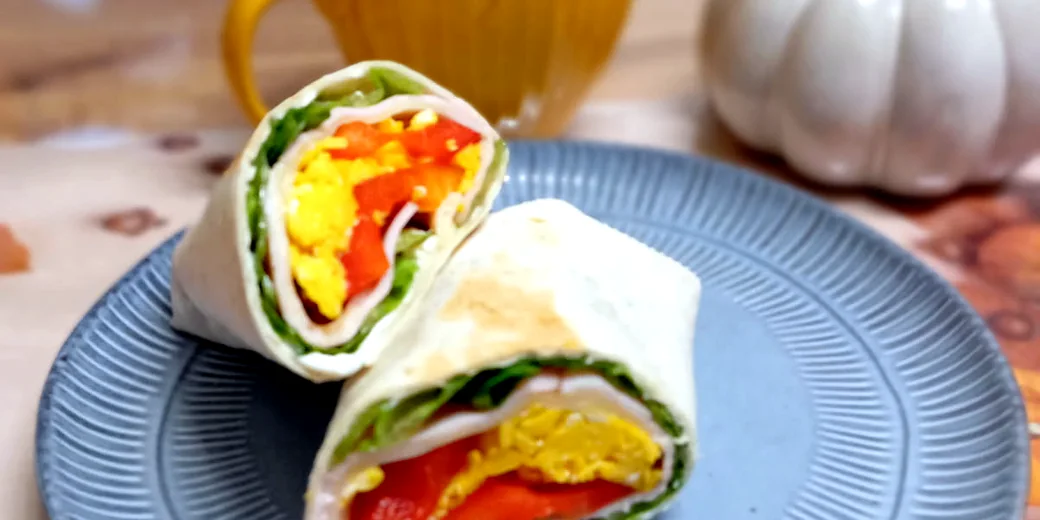 Wrap z indykiem, jajkiem, papryką i sałatą, podany na talerzu z herbatą